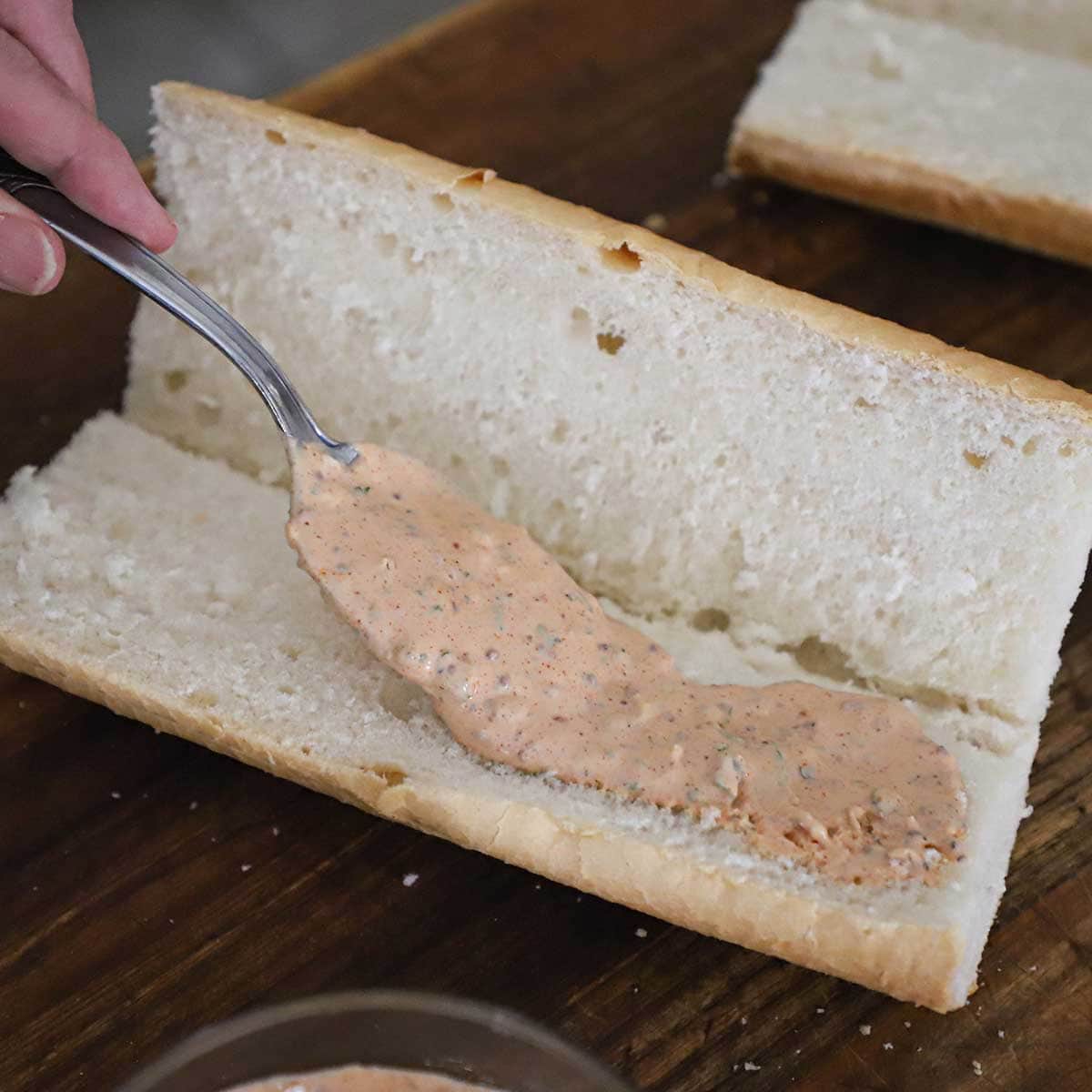 A person using a spoon to spread a layer of cut and opened up.