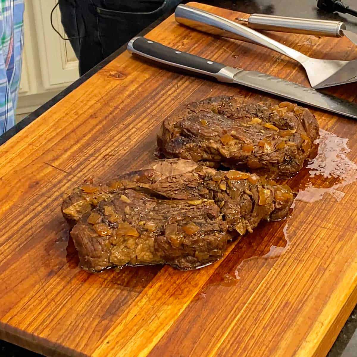 Two large chuck roasts that have been slow cooker in a Crockpot for hours and are resting on a wooden cutting board.
