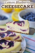 A person using a cake spatula to lift a slice of lemon blueberry cheesecake from a the cake resting on a circular white cake dish.