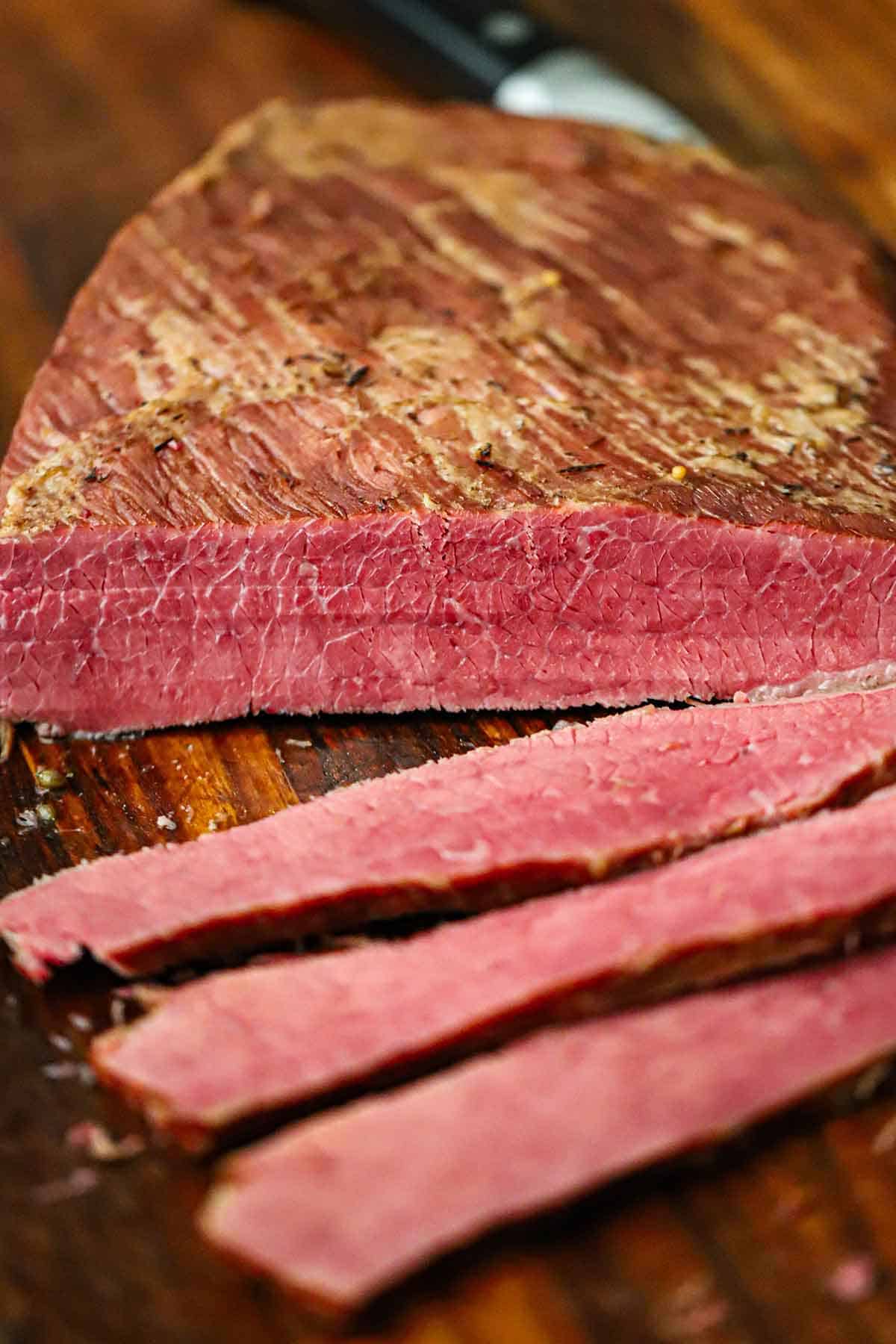 A close-up view of a classic homemade corned beef with several slices revealing the bright red interior of the meat.