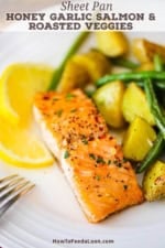 A close-up view of a fillet of roasted honey garlic salmon next to oven-roasted potatoes and green beans and a couple slices of lemon.