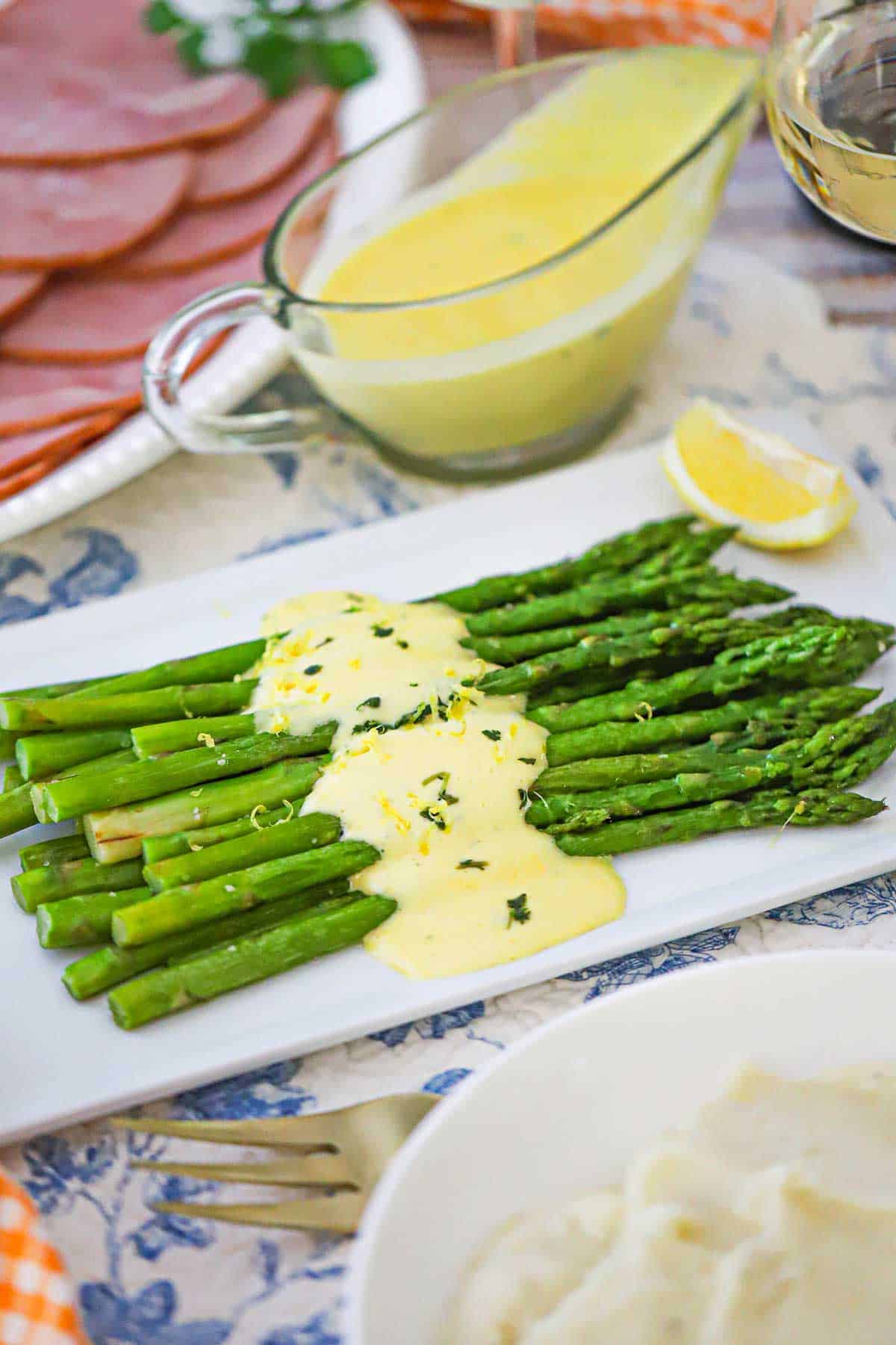 A rectangle white platter filled with Asparagus with Béarnaise Sauce with a glass gravy boat filled with the Béarnaise sauce.