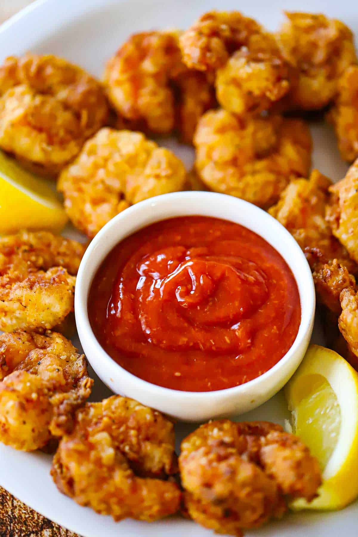 A white dinner plate filled with crispy Southern fried shrimp surrounding a small white bowl filled with homemade cocktail sauce.