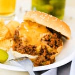 A close-up view of Homemade Sloppy Joes with melty cheddar cheese over the top of the filling sitting on a white dinner plate.