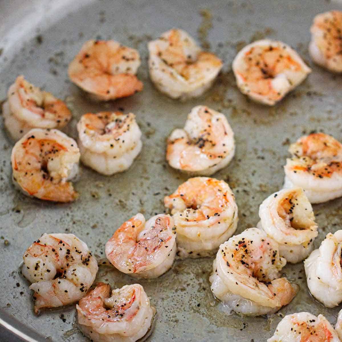 A close-up view of seasoned shrimp being sautéed in oil in a large stainless steel skillet.