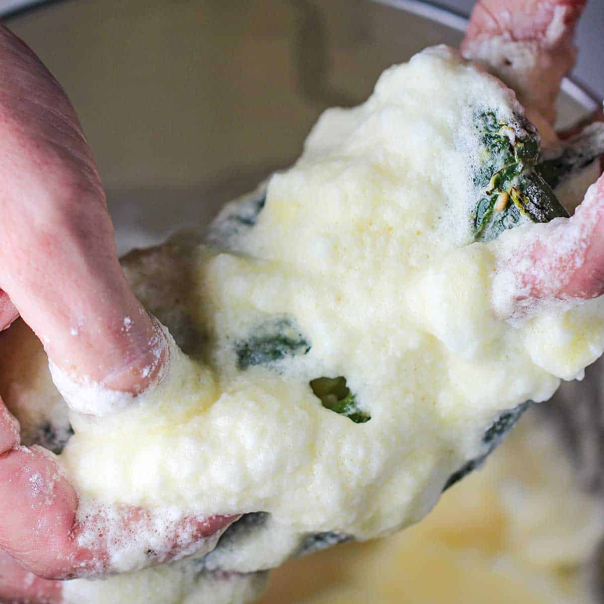 A person holding a stuffed roasted poblano that has been submerged into an egg batter.