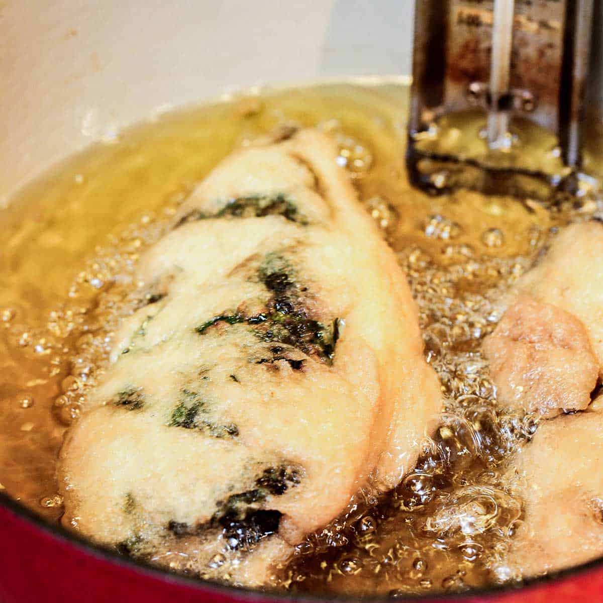 Two egg batter breaded chiles being fried in hot oil in a large Dutch oven pot.