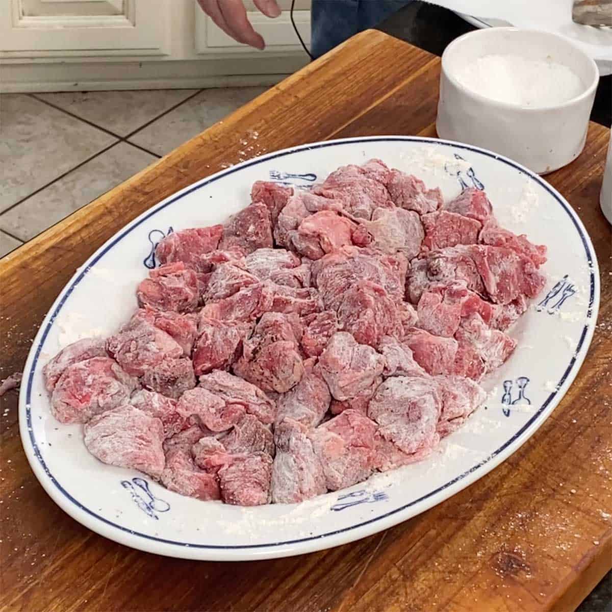 A large platter filled with chunk of chuck roast that have been seasoned with salt and pepper and toss with flour.