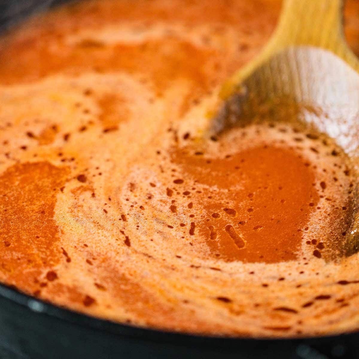 A close-up view of a thin Mexican red sauce simmering in a black cast-iron skillet.