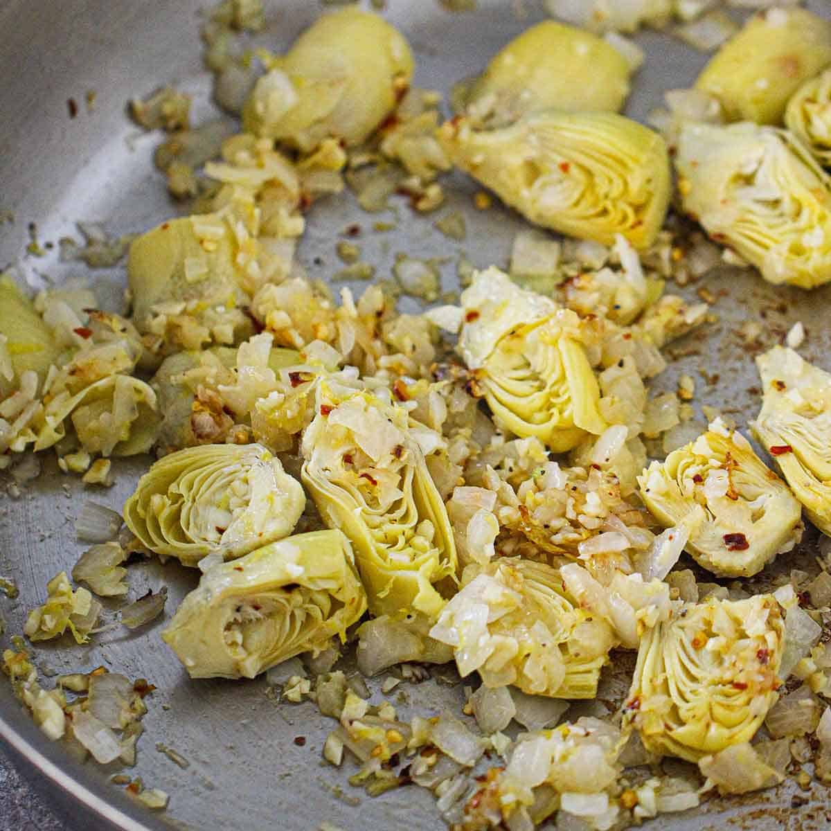 Artichoke hearts, onion, garlic, lemon zest, and red pepper flakes being sautéed in oil in a large skillet.
