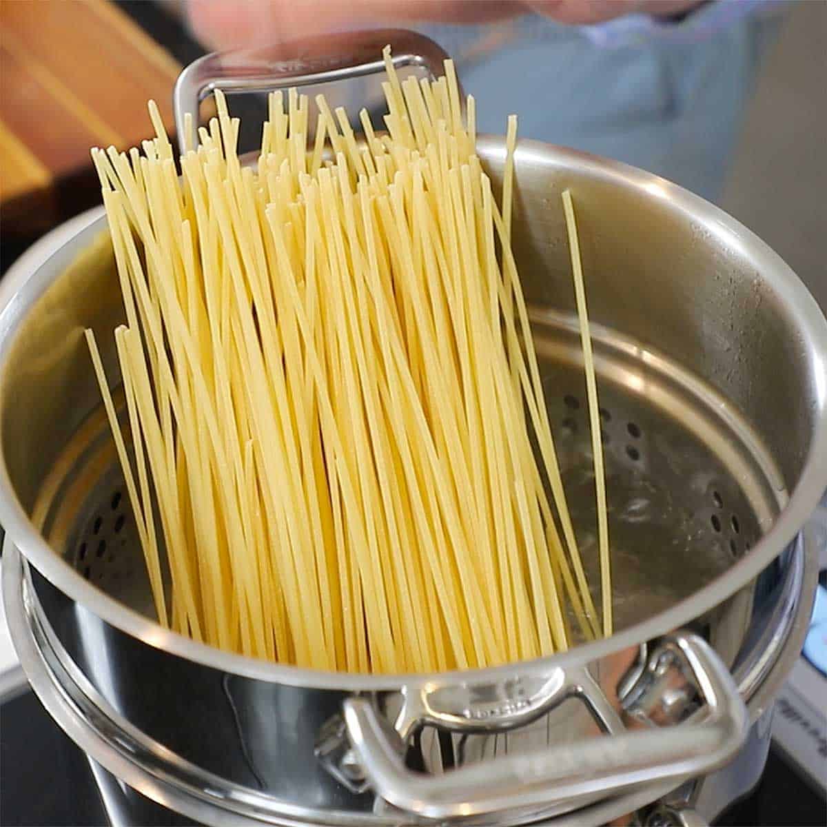 Uncooked linguine pasta resting upright in a pasta pot filled with boiling salted water.