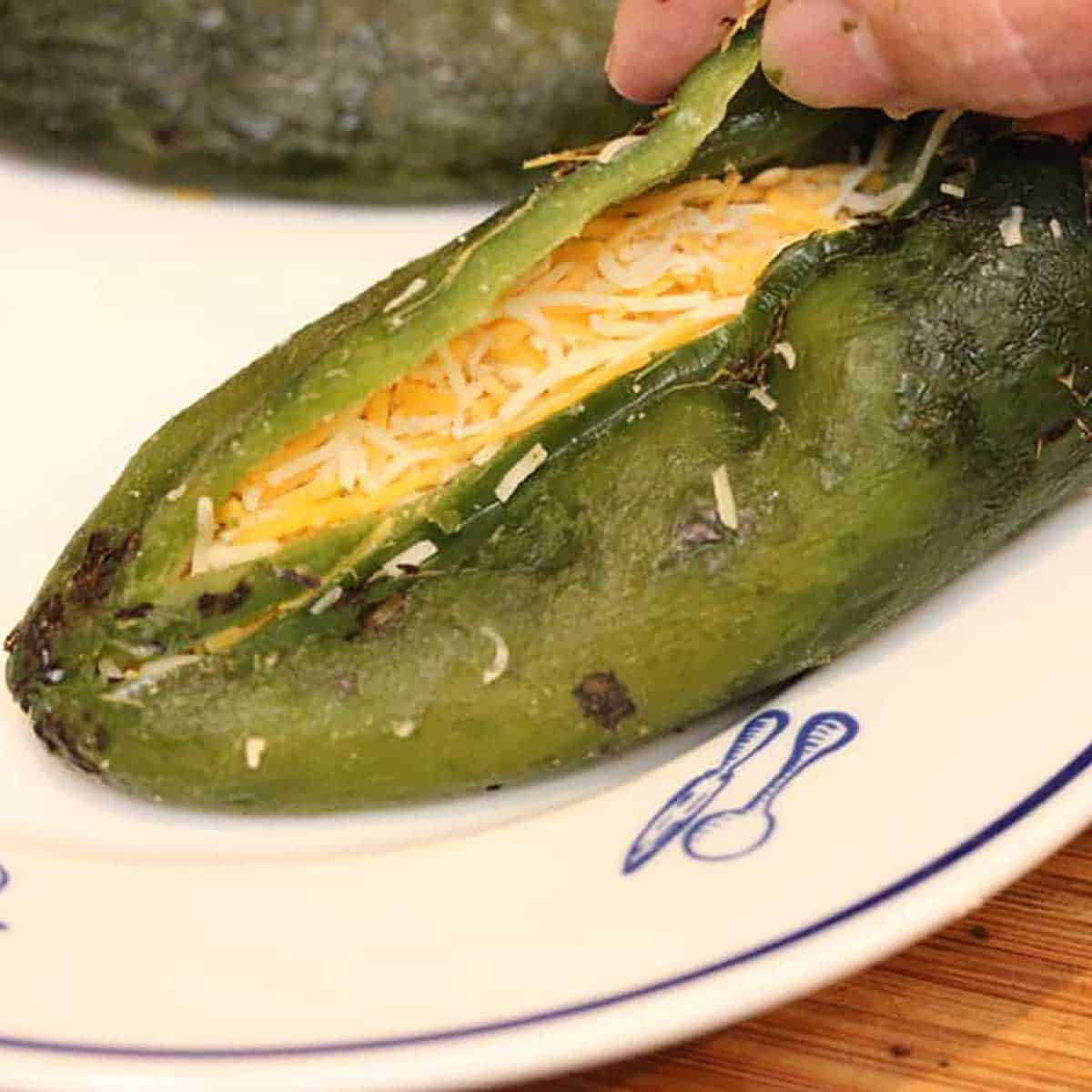 A person using his thumb and finger to close a roasted poblano chile that has been split open and filled with shredded cheese.