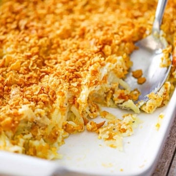 A close-up view of hashbrown casserole from scratch in a white baking dish with a portion of the casserole missing.
