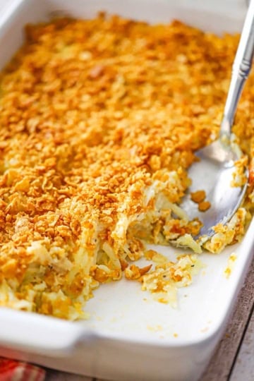 A hashbrown casserole from scratch in a white baking dish with a portion of the casserole missing.