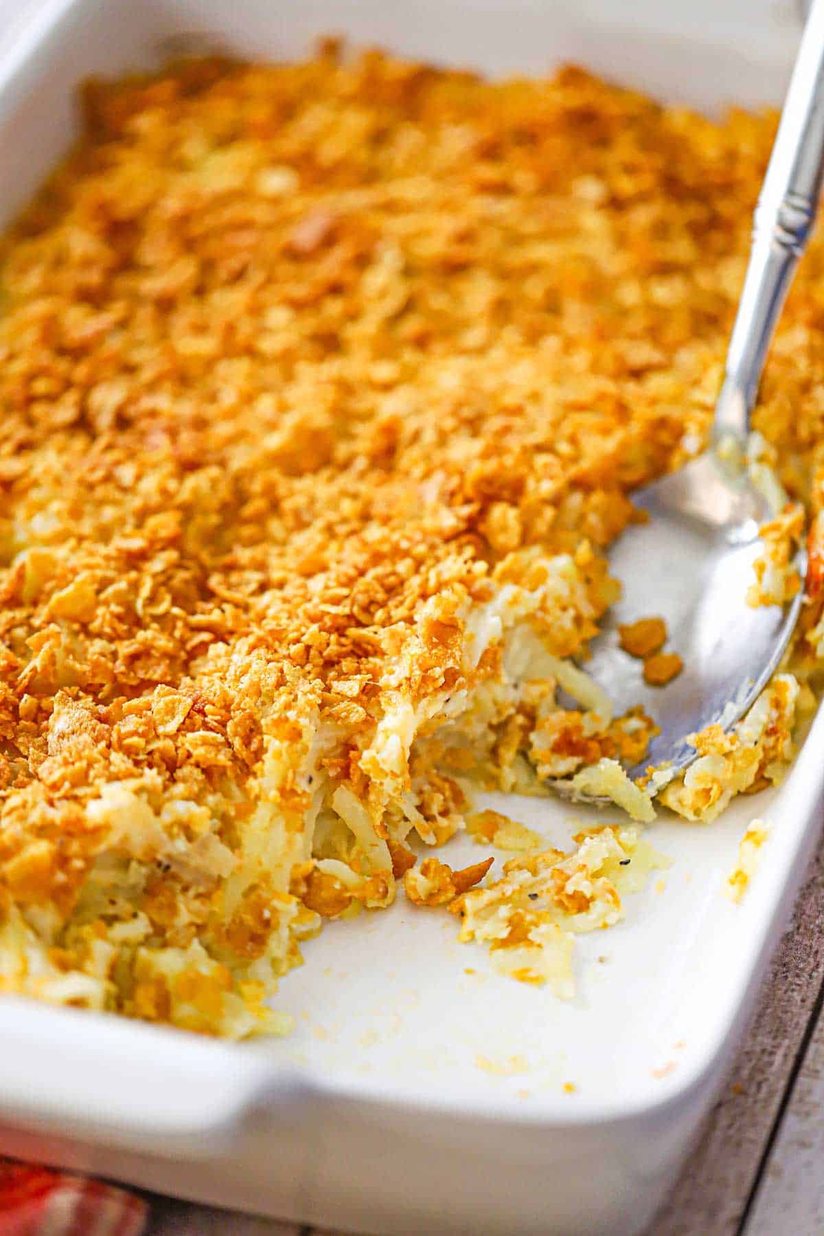 A hashbrown casserole from scratch in a white baking dish with a portion of the casserole missing.