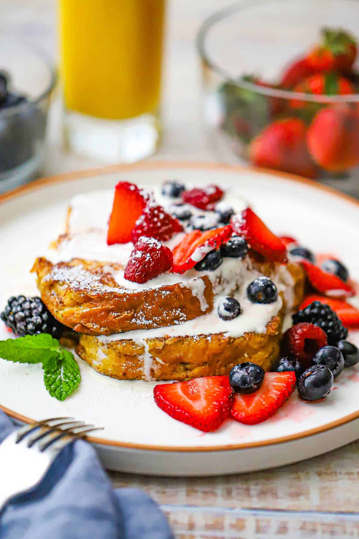 A large white dinner plate filled with two caramelized brioche French toast slices that are topped with a mascarpone cream sauce and macerated berries.