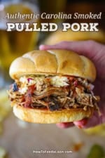A person holding a smoked pulled pork sandwich with one hand revealing the shredded pork, BBQ sauce, and coleslaw on toasted buns.