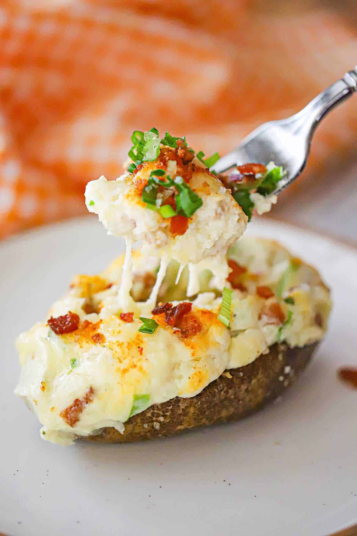 A person using a fork to lift the filling out of a twice baked potato that is resting on a white salad plate.
