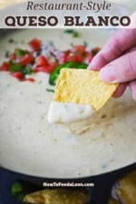 A person holding a triangular corn tortilla chip that he just dipped into a skillet filled with white queso blanco.