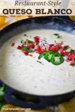 A cast-iron skillet filled with queso blanco and garnished with pico de gallos, sliced peppers, and chopped cilantro.