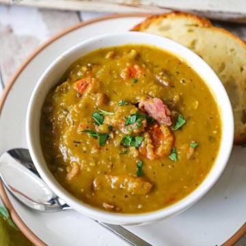 An overhead view of a soup bowl filled with split pea soup with ham bone garnished with chopped Italian parsley and chunks of crispy ham.