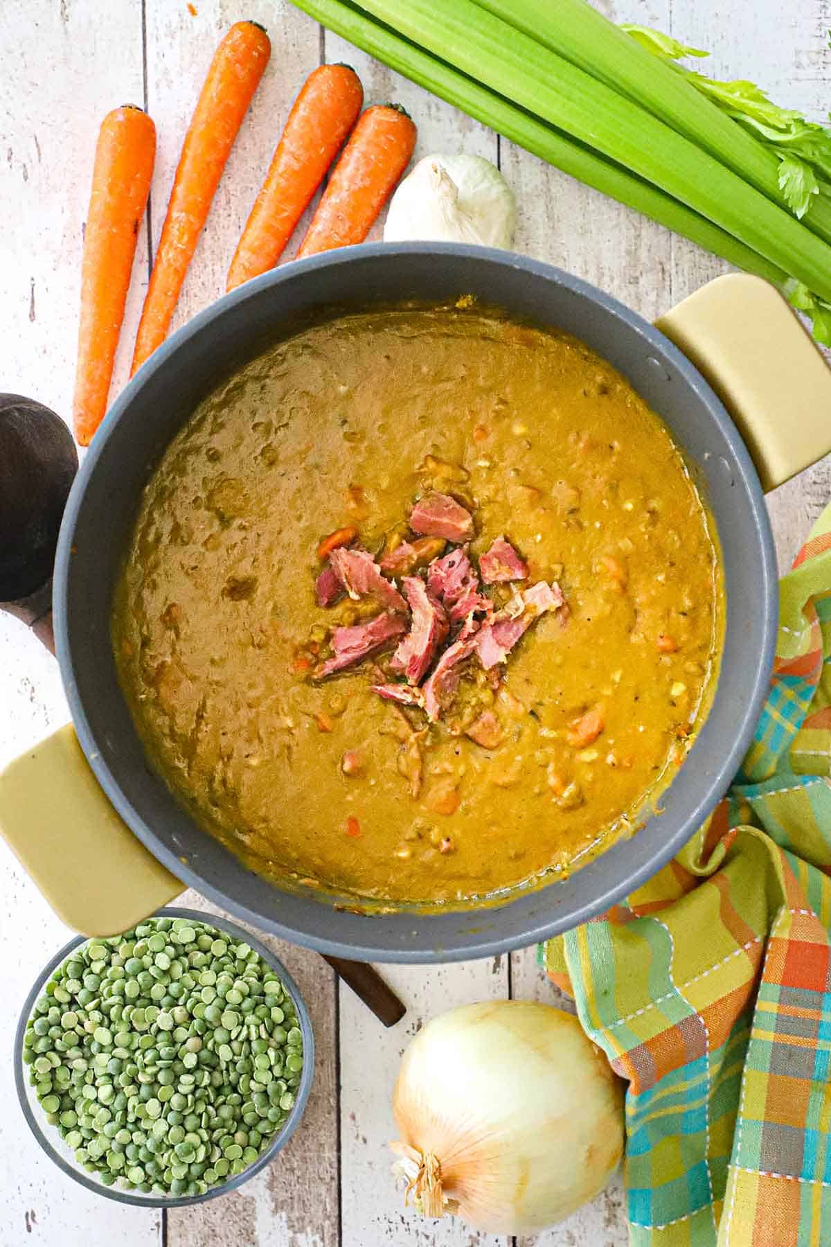 An overhead view of a large circular pot filled with homemade split pea soup with a mound of crispy ham in the center of the soup.