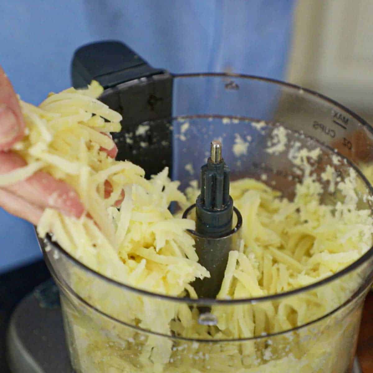 A person lifting strings of par-boiled potatoes that have been shredded in a food processor.