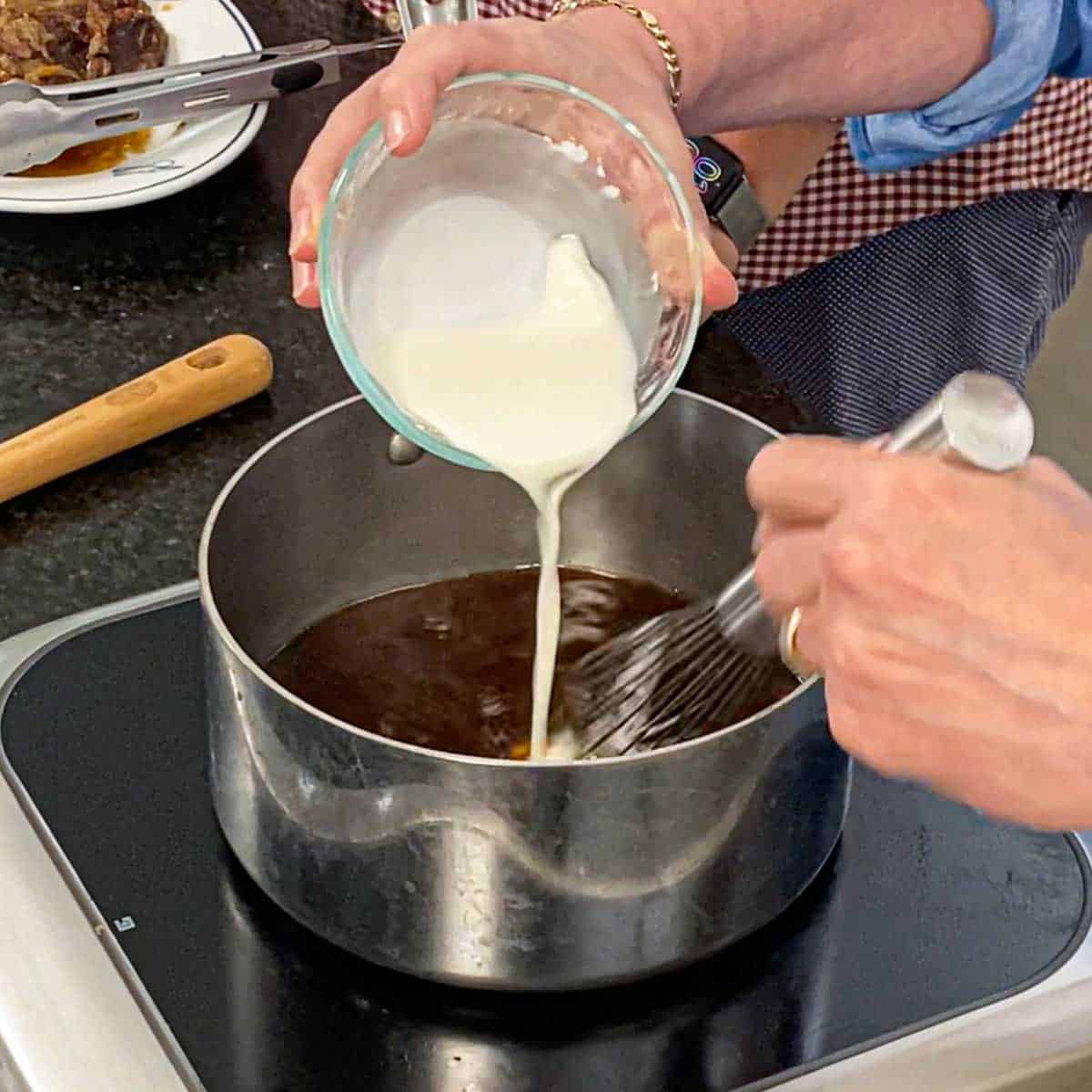 A person pouring a cornstarch slurry into a saucepan that is filled with a strained liquid from a slow cooker beef Manhattan.