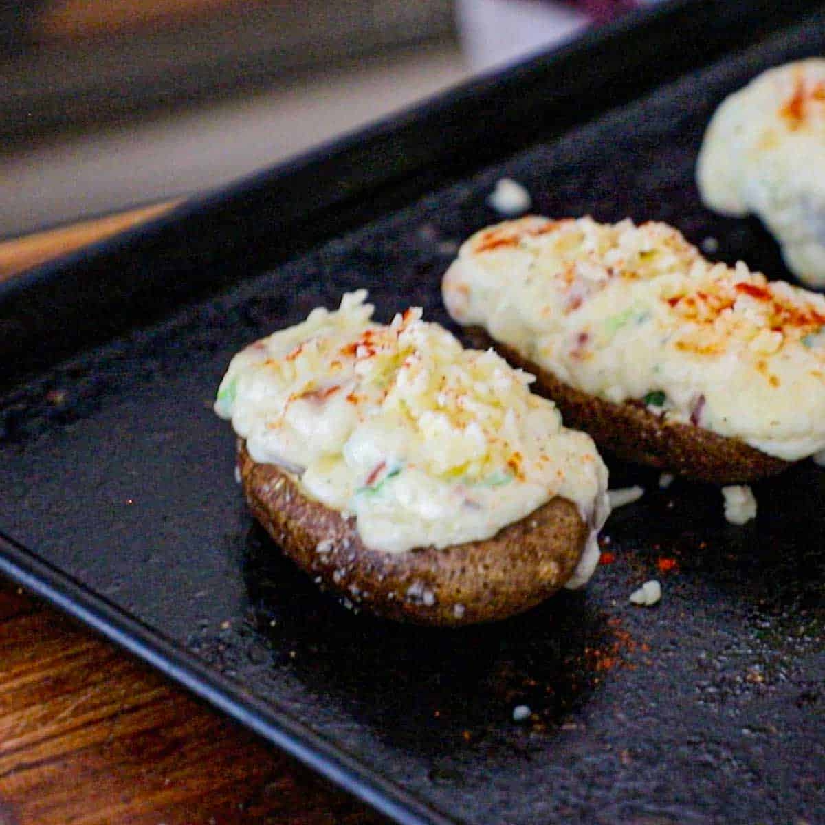 A line-up of twice baked potatoes topped with white cheddar cheese and smoked paprika on a metal baking sheet.