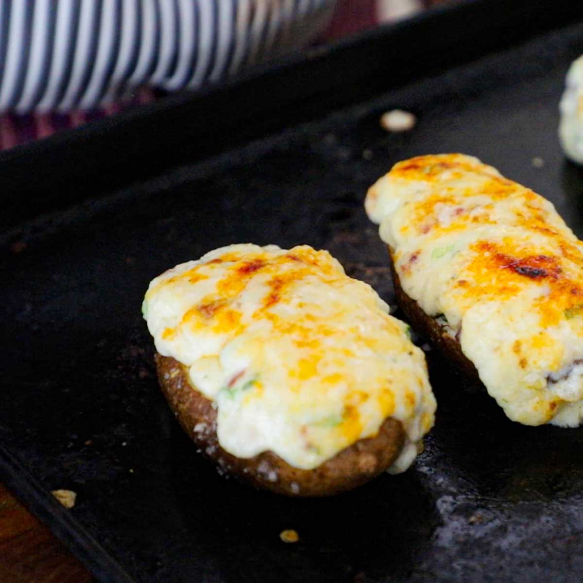 A line-up of twice baked potatoes topped with melted white cheddar cheese and smoked paprika on a metal baking sheet.