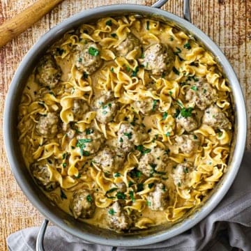 An overhead view of a large stainless steel skillet filled a freshly prepared Swedish meatball pasta topped with chopped Italian parsley.
