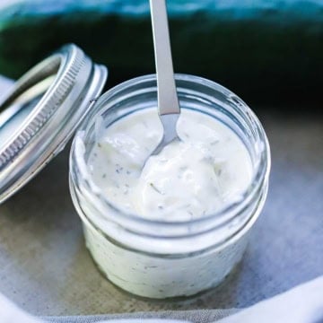 A close-up view of a spoon inserted into a small jar filled with homemade tzatziki sauce.