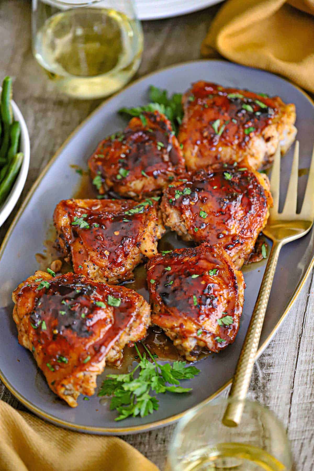 An oval platter filled with six pieces of Baked Brown Sugar Chicken Thighs with a gold serving fork nearby.