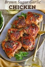 An oval platter filled with six pieces of Baked Brown Sugar Chicken Thighs with a gold serving fork nearby.
