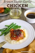 A baked brown sugar garlic chicken thigh resting on a bed of mashed potatoes next to a small pile of green beans all on a white dinner plate.