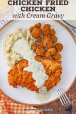 An overhead view of a white dinner plate filled with a serving of chicken fried chicken with cream gravy, fried okra, and mashed potatoes.