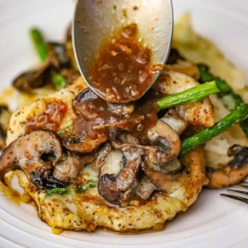 A spoon being used to drizzle a brown sauce over the top of a serving of chicken Madeira with mushrooms and asparagus.