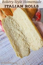 A person holding a homemade Italian roll that has been split open lengthwise revealing the soft crumb interior of the bread.