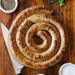 An overhead view of a circular rope of homemade Italian sausage the has been cooked and seared and is resting on a wooden cutting board.
