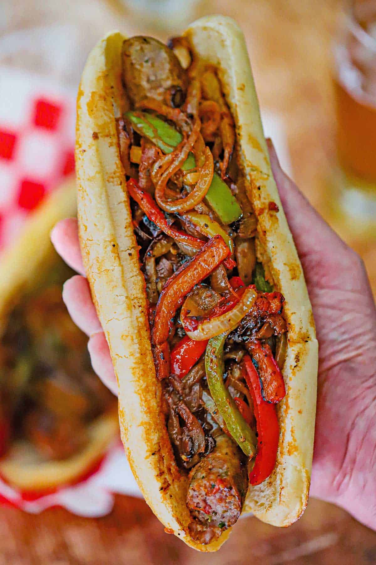 A person holding a large NYC-Style Sausage and Peppers in an Italian roll in the palm of his hand.