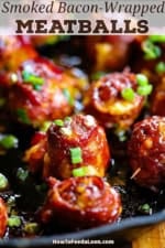 A close-up view of smoked bacon-wrapped meatballs with cheddar and jalapeño in a cast-iron skillet with chopped scallions sprinkled on top.