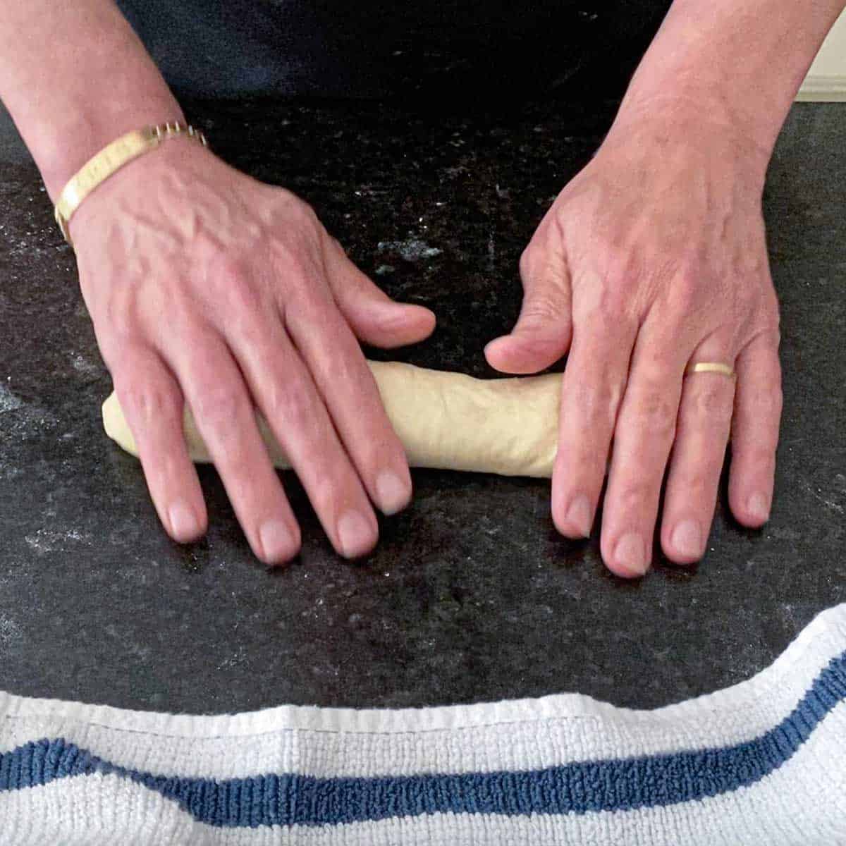 A person using the palms of his hands to gently roll a tubular piece of dough into a 6-inch cylinder.