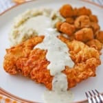 A close-up view of Southern chicken fried chicken with cream gravy on a white dinner plate along with mashed potatoes and gravy and fried okra.