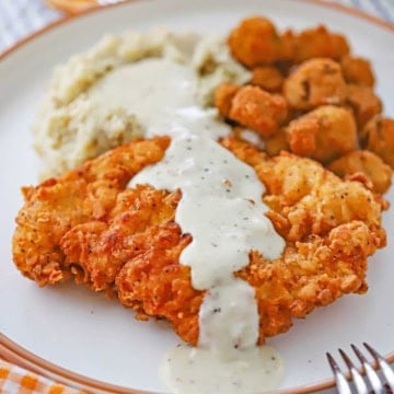 A close-up view of Southern chicken fried chicken with cream gravy on a white dinner plate along with mashed potatoes and gravy and fried okra.