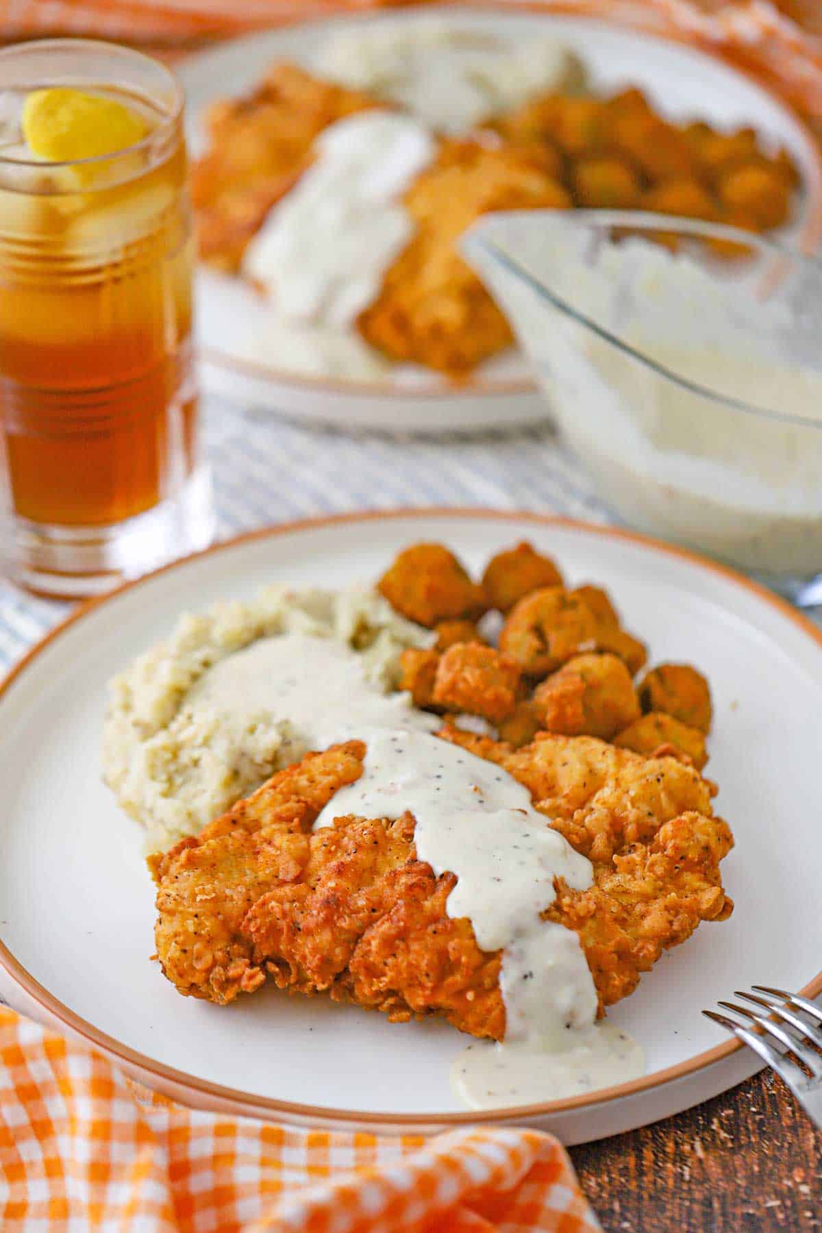 Two white dinner plates filled with servings of Southern Chicken Fried Chicken with Cream Gravy, mashed potatoes, and fried okra.