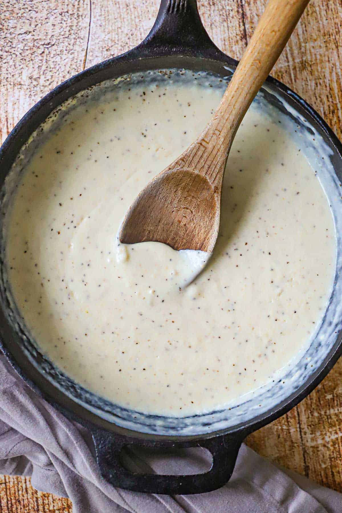 An overhead view of Classic Cream Gravy in a black cast-iron skillet with a wooden spoon resting in the middle of the pan.