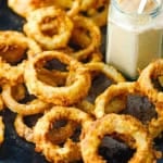 A pile of steakhouse onion rings on a baking pan with a jar or Cajun remoulade also on the pan.