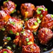 A cast-iron skillet filled with smoked bacon-wrapped meatballs with cheddar and jalapeño, topped with chopped scallions.
