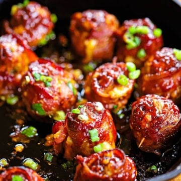 A cast-iron skillet filled with smoked bacon-wrapped meatballs with cheddar and jalapeño, topped with chopped scallions.
