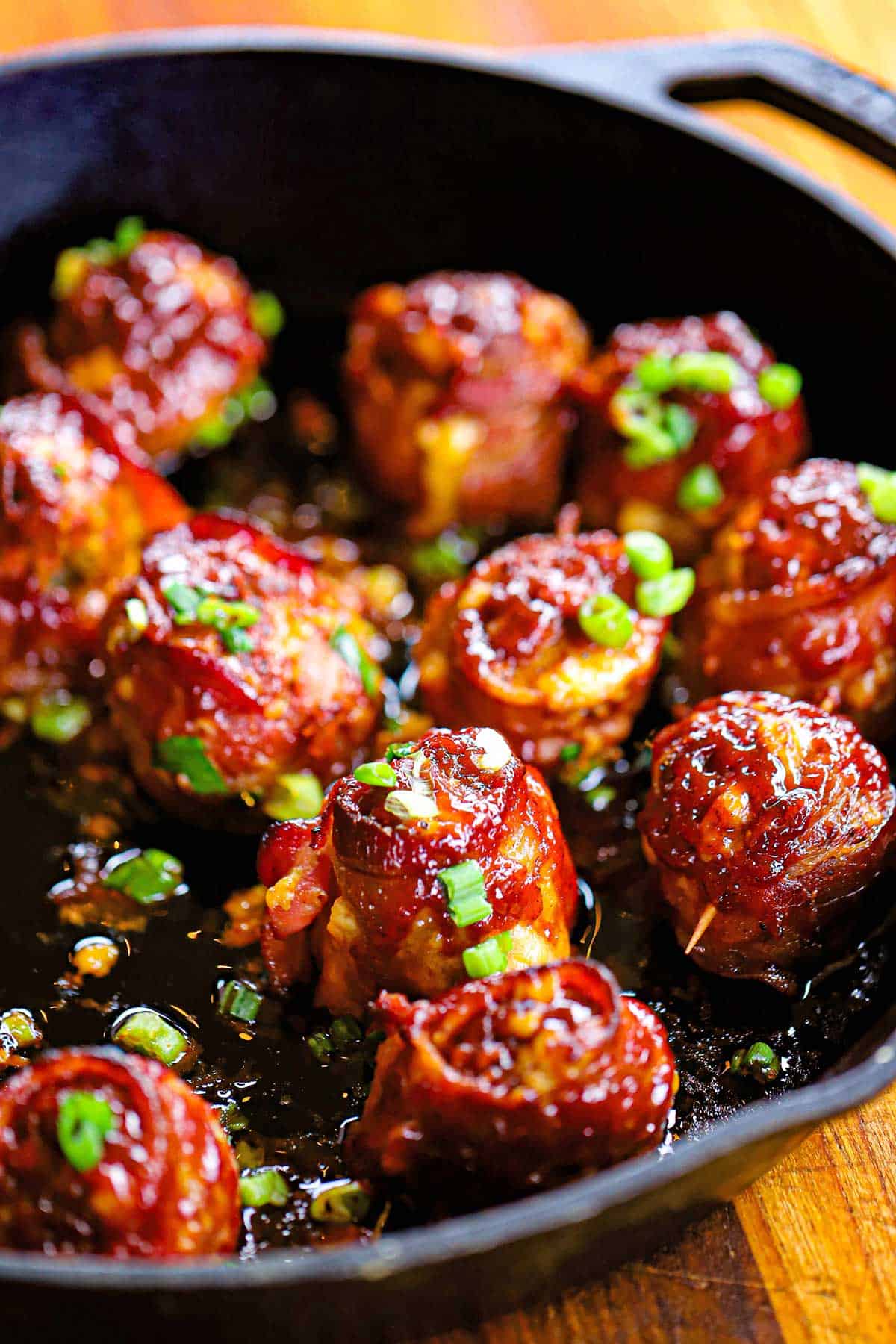 A cast-iron skillet filled with smoked bacon-wrapped meatballs with cheddar and jalape&ntilde;o, topped with chopped scallions.